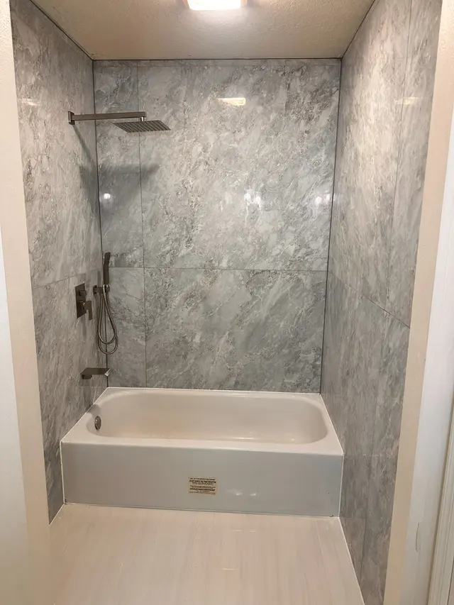 Finished bathroom with a marble look tile tub surround, a rain shower head and a built in niche