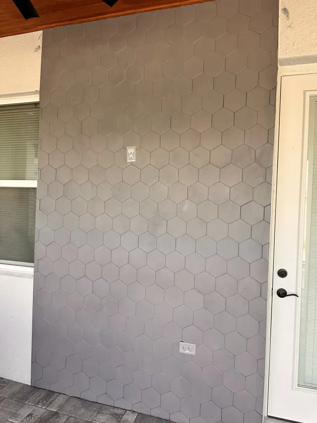 Exterior wall finished in hexagon tile next to a white entry door