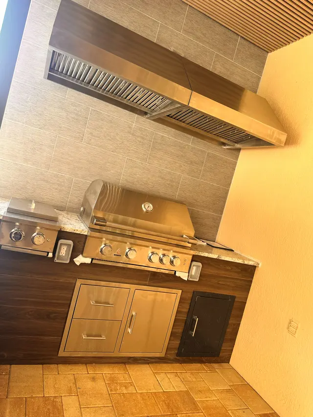 Outdoor kitchen detail with a stainless grill, vent hood and stone counter