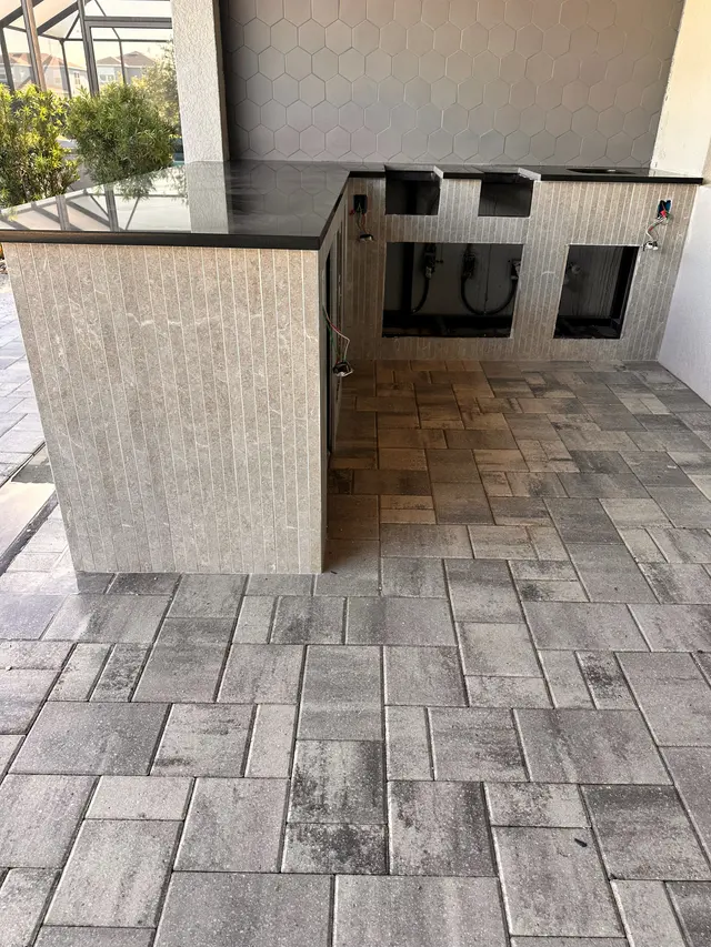 Outdoor kitchen island and paver patio under a screened enclosure