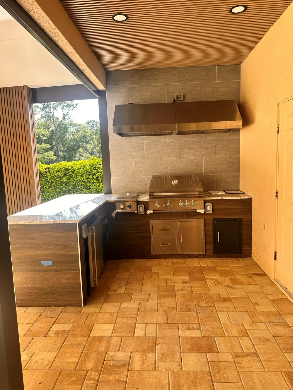 Outdoor kitchen built by B2B Construction, with a built in grill under a wood plank ceiling