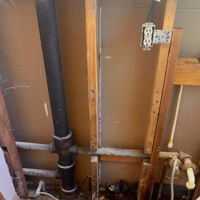 Open bathroom wall during rough in, with the cast iron drain stack, water lines and an outlet box mounted on the framing