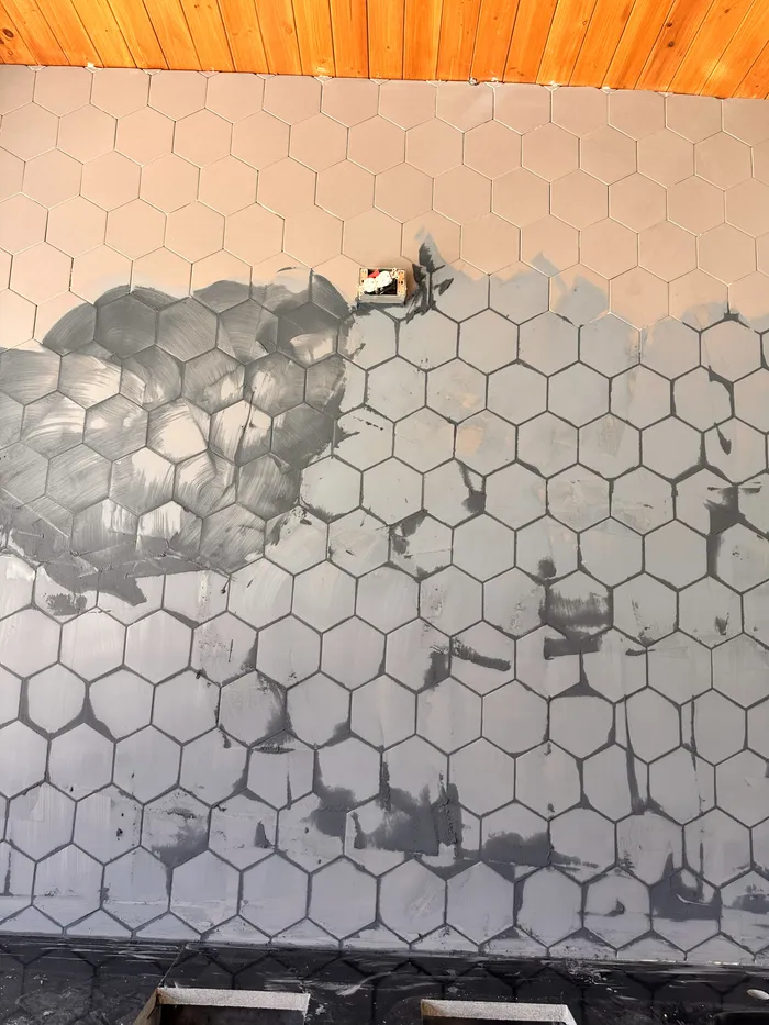 Hexagon tile going up on a wall, half set, with the substrate still visible